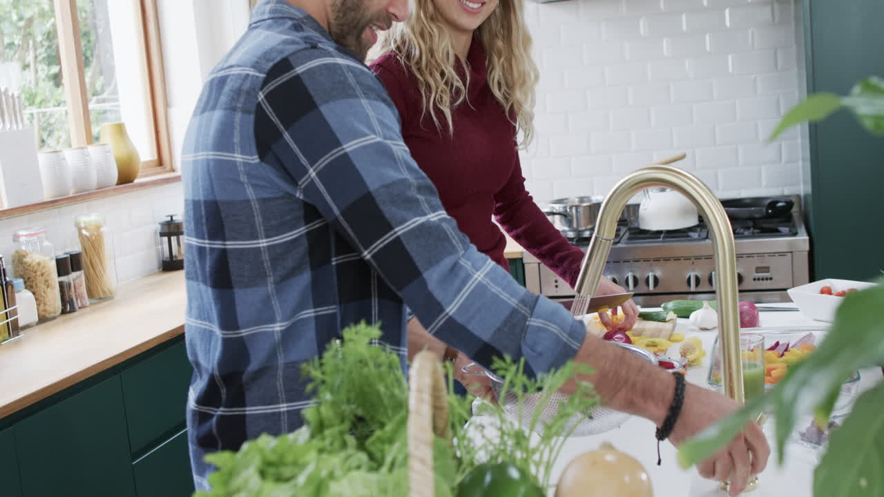 Casal diverso feliz preparando o jantar na cozinha de casa, em câmera lenta.