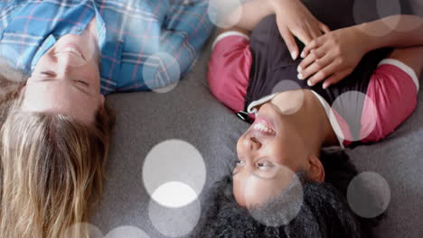 animación de puntos de luz sobre dos niñas adolescentes felices y diversas acostadas en la cama hablando