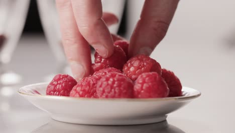 detalle dedo agarrando trozos de frambuesa de un plato mientras cocina un postre dulce comida saludable primer plano