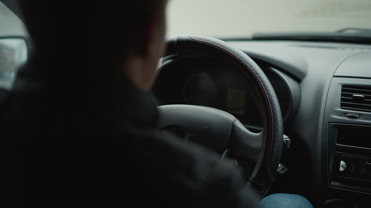 Back view of vehicle owner driving with hands on steering wheel, interior shadow framing driver silhouette against blurred windshield, capturing urban commute mood and focused control