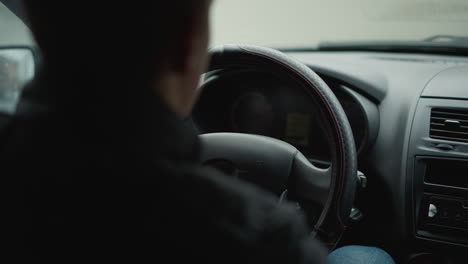 back view of vehicle owner driving with hands on steering wheel, interior shadow framing driver silhouette against blurred windshield, capturing urban commute mood and focused control