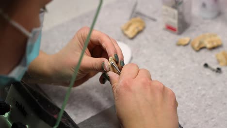 carving out and refining an artificial tooth implant by masked dental worker in small healthcare clinic at the work-shop