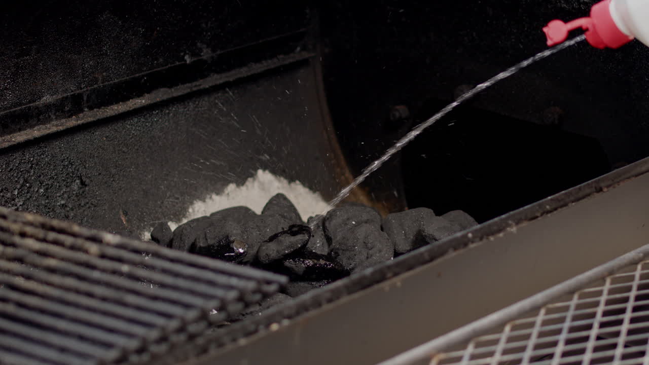 Lighter fluid being sprayed on to charcoal briquettes in BBQ pit smoker