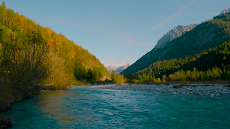 Río-De-Montaña-Con-Agua-Azul-Clara-Corriendo-Por-Vibrantes-Y-Coloridos-árboles-Otoñales-Bajo-El-Sol