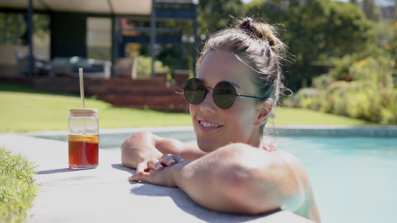 Relaxing in pool, woman smiling with sunglasses and iced tea on sunny day