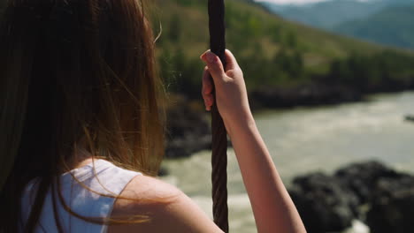 woman holds of rope standing on bridge over mountain creek