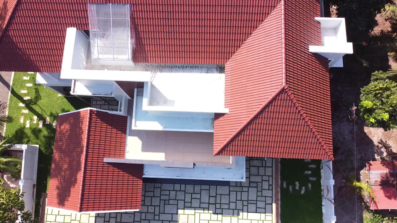 Aerial drone view of a modern Kerala home in India with sloping tiled roof, spacious balcony, green lawn, and elegant architecture surrounded by tropical trees and serene natural environment