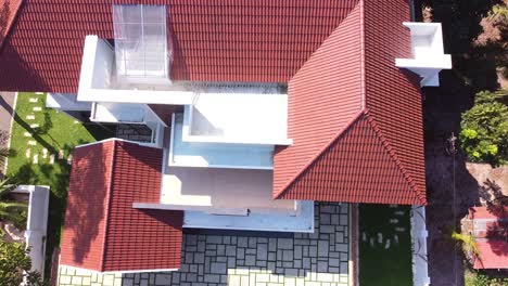 aerial drone view of a modern kerala home in india with sloping tiled roof, spacious balcony, green lawn, and elegant architecture surrounded by tropical trees and serene natural environment