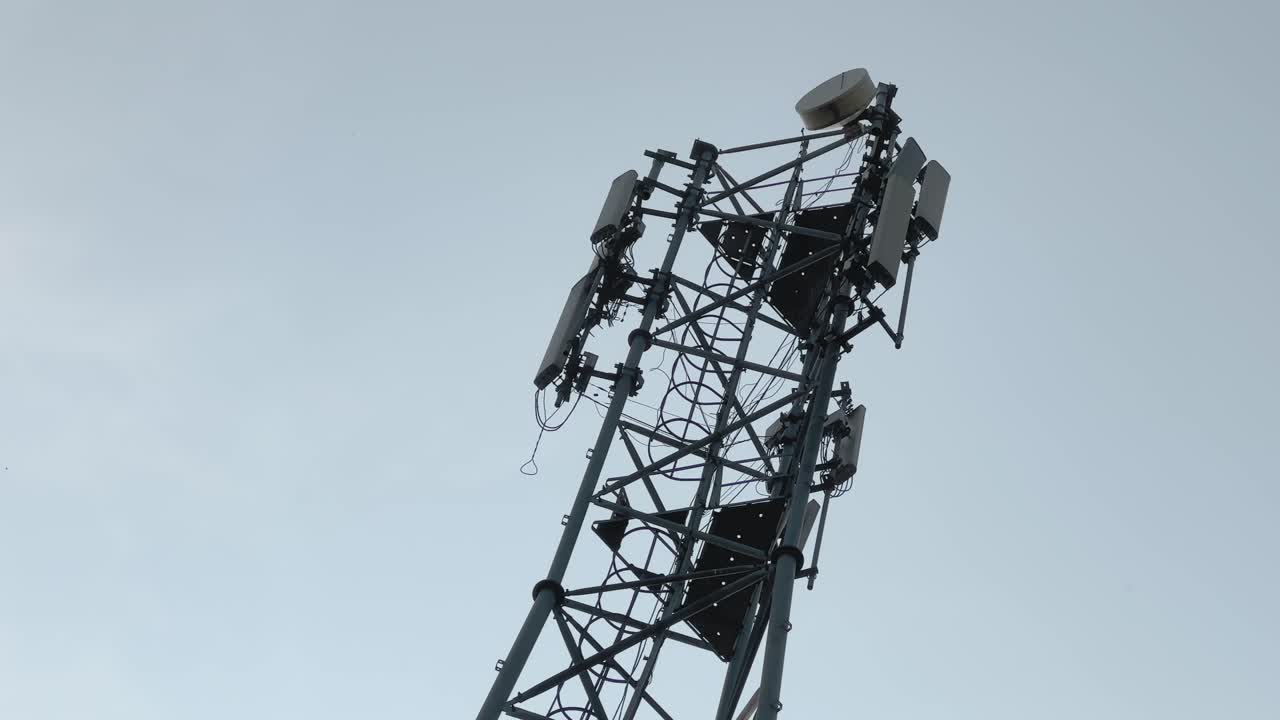 Low angle view of mobile communication tower rising into clear sky, antennas and cables forming strong geometry, symbolizing connectivity, technology, and infrastructure