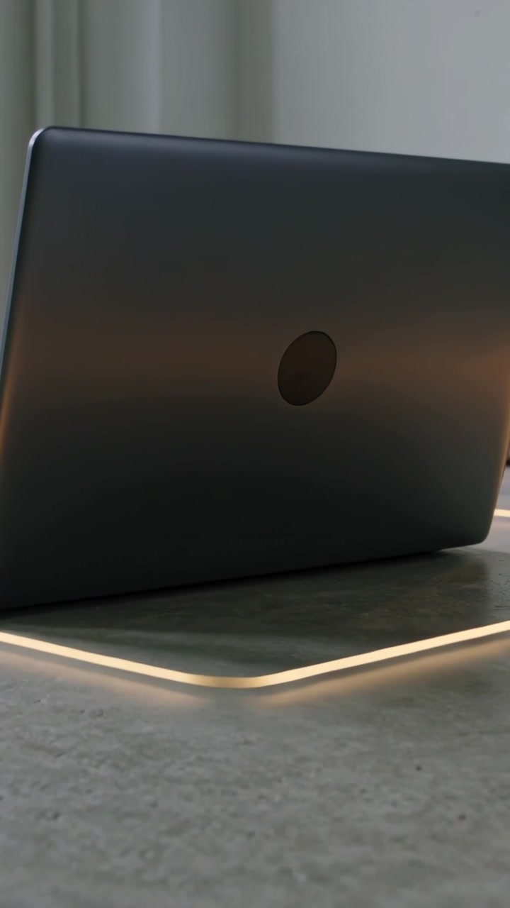 Video verticale: Tavoletta luminosa che inizia a delineare un laptop chiuso con logo circolare su una scrivania vicino a una tenda.