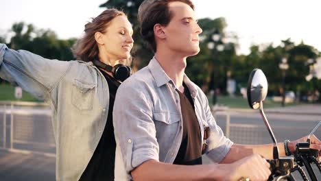 young couple enjoying riding on electric minibike through park in summer. happy trendy couple spending time together. park side