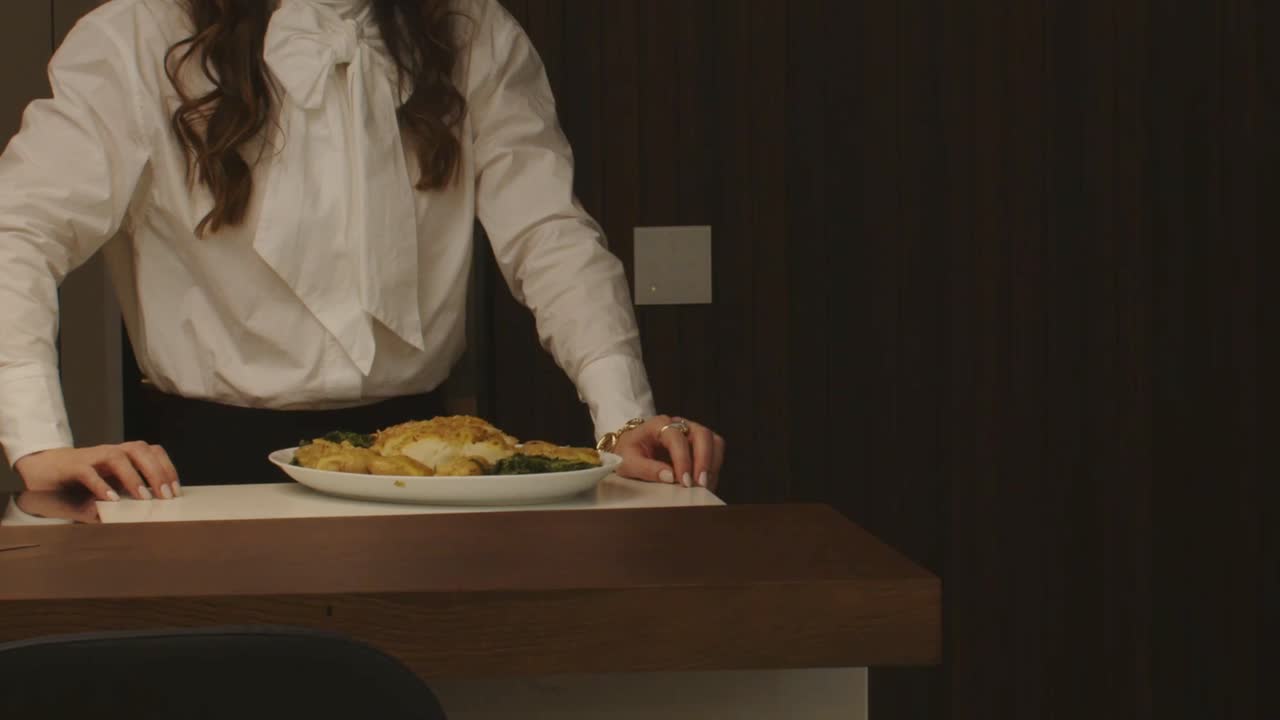 Woman in white blouse presenting a dish with golden crusted food at a counter