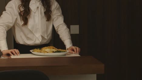 woman in white blouse presenting a dish with golden crusted food at a counter