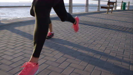 Zwei-Sportliche-Frauen-Laufen-Im-Freien-In-Zeitlupe-Auf-Der-Promenade-Bei-Sonnenuntergang-Am-Meer-Und-Genießen-Den-Abendlauf