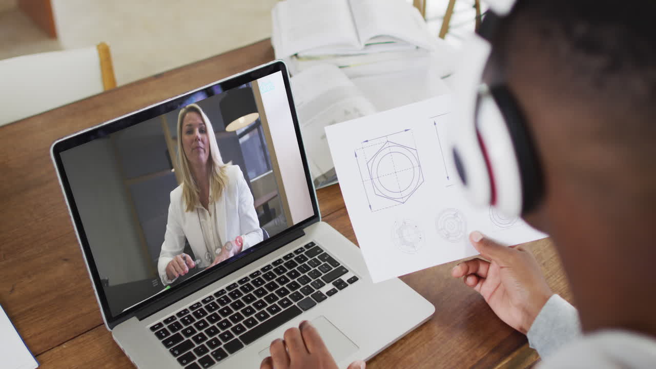 estudiante universitario afroamericano que sostiene notas mientras hace una videollamada en una computadora portátil en casa