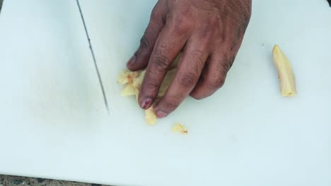 el jengibre cortado , pelado se corta en pequeños trozos usando un cuchillo en un tablero de compras , cocina tradicional al aire libre