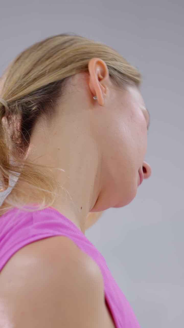 vista lateral de un atleta practicando una torsión del cuello en una habitación minimalista vista parcial de otra mujer a un lado y un enchufe arrancado ligeramente visible en el fondo