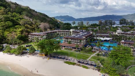 drone footage captures a luxury resort by the beach in phuket, thailand, showcasing lush greenery, pools, and scenic ocean views