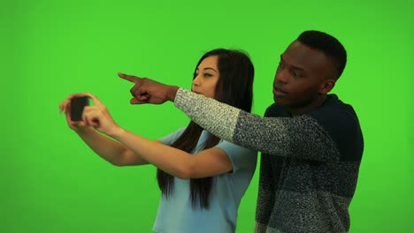 una joven asiática y un joven negro toman fotos de su entorno - estudio de pantalla verde