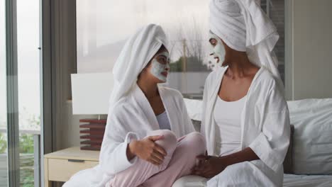 Video-of-relaxed-diverse-female-friends-moisturizing-with-face-masks-and-talking-in-bathroom