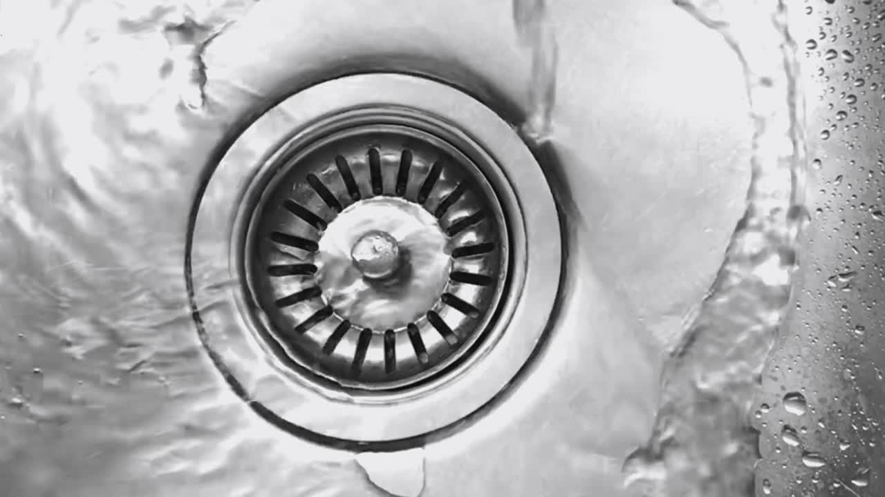 Close up view from above of water pouring into a stainless steel sink