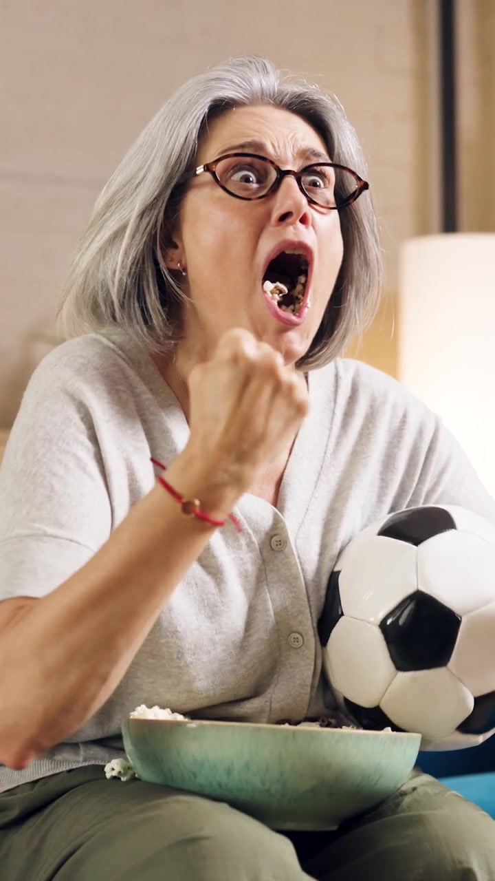 Donna matura che guarda una partita di calcio e festeggia un gol sul divano