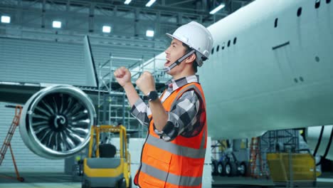 vista lateral de un ingeniero masculino asiático con casco de seguridad de pie y gritando meta celebrando trabajando con aviones en el hangar