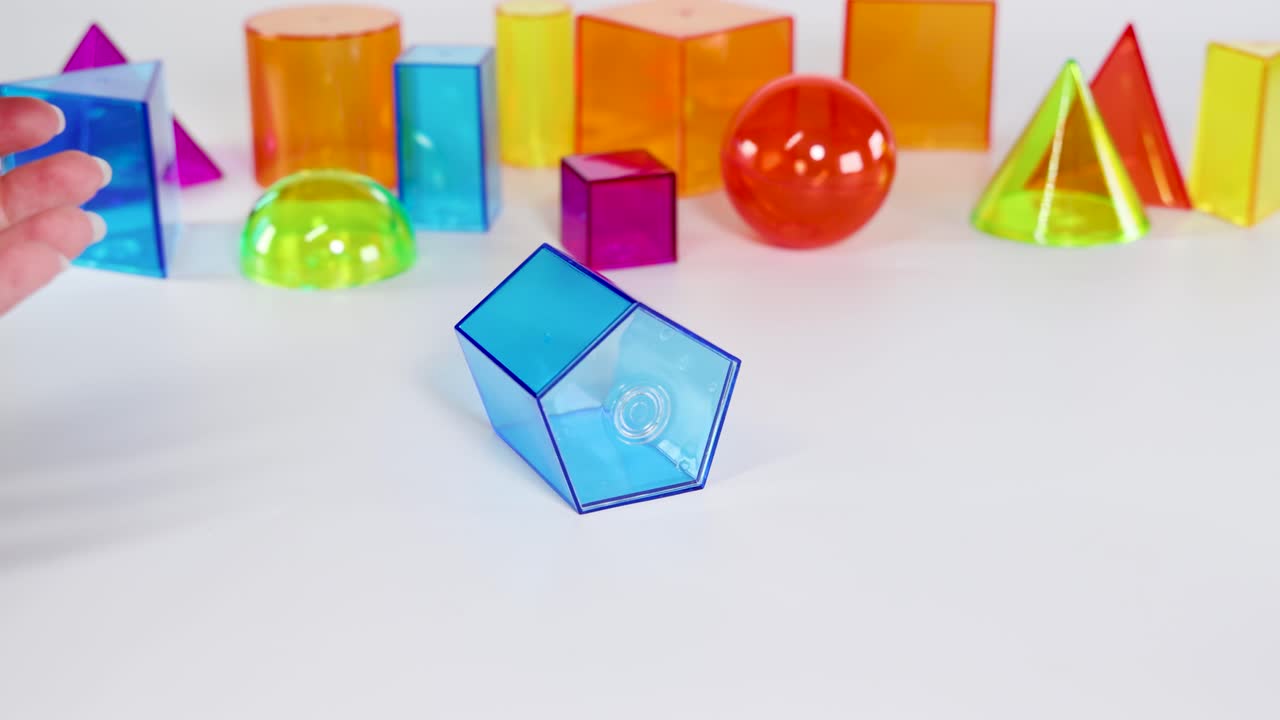Hands interact with vibrant 3D shapes on a white surface, demonstrating movement and balance in a well-lit environment