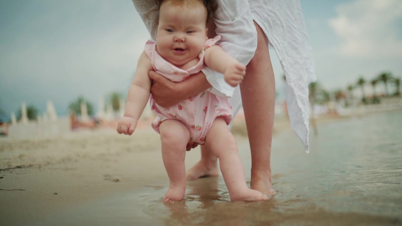 Ung mor holder baby nær en rolig strandlinje under ferie med mykt lys.