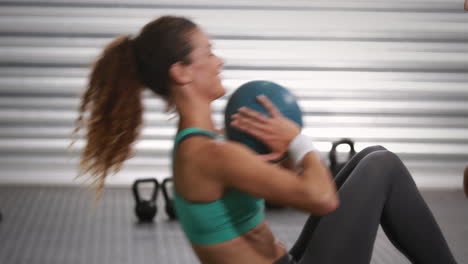 Woman-doing-sit-ups-with-trainer-at-crossfit-gym