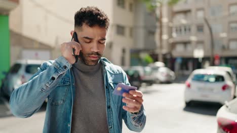 young arab man talking on the smartphone and using credit card at street