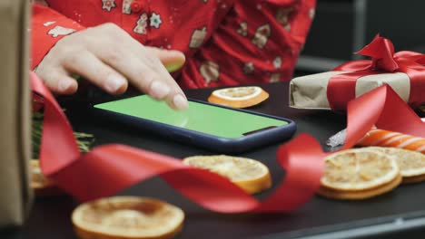 smartphone with green screen on background of christmas tree and holiday lights. chroma key. christmas online shopping. hands using smartphone with green screen watching christmas present