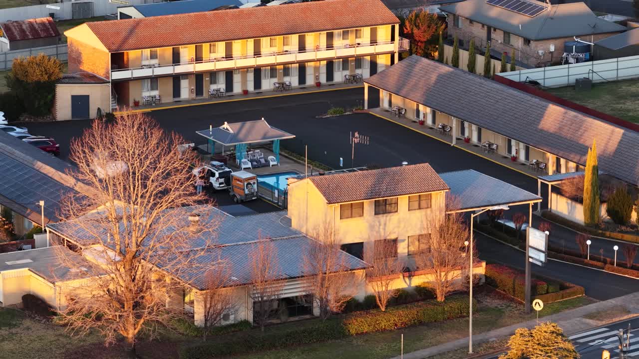 Aerial camera smoothly pans over a motel complex and empty street in Coonabarabran, Australia, bathed in warm sunset light with visible smoke haze