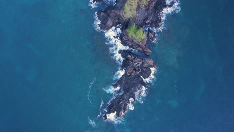 aerial tracking shot of deep blue ocean and dark cliffs with green vegetation in the philippines