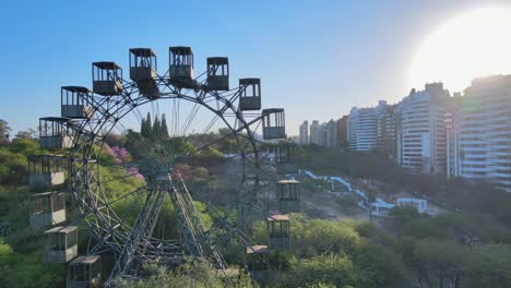 Aerial-panning-view-capturing-vuelta-al-mundo-de-cordoba-ferris-wheel-and-landmark-stairway-leading-to-hilltop-observation-deck-in-parque-sarmiento-at-daytime-with-glowing-sun-in-the-sky