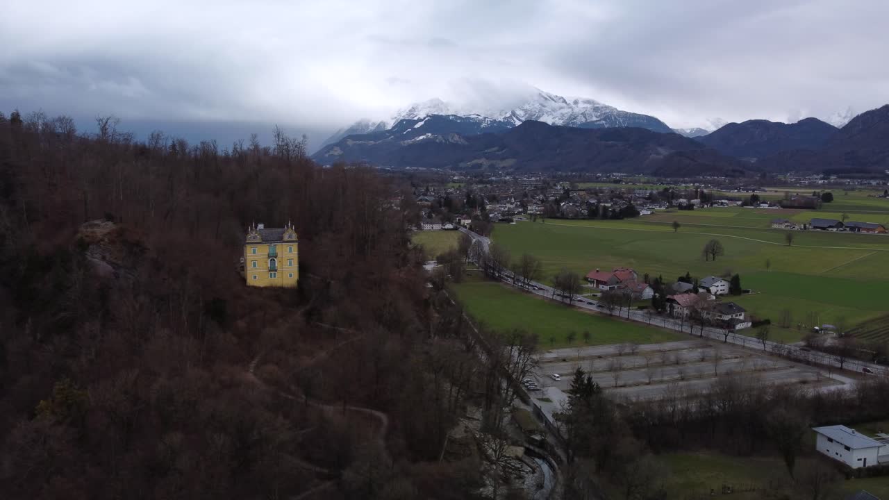 toma de órbita aérea cinematográfica del campo de austria, mostrando casas tradicionales pintorescas en primer plano y montañas nevadas en el fondo