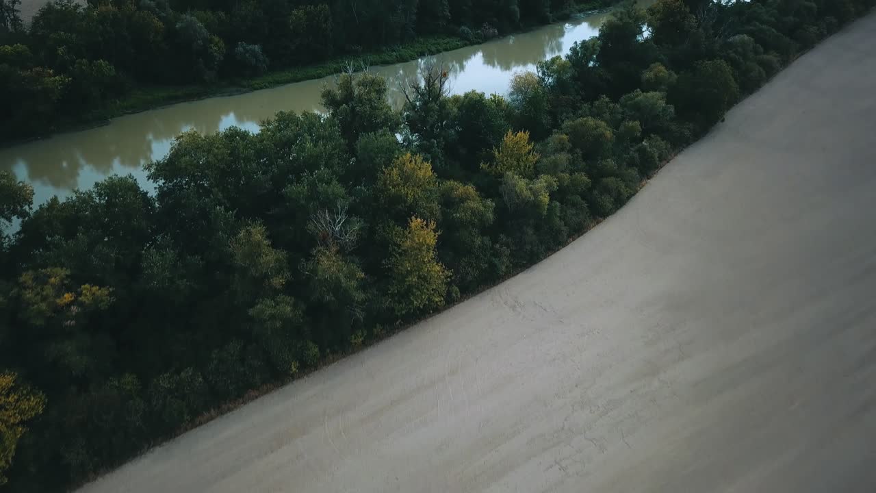 Drone shot over slow muddy river between fields and trees