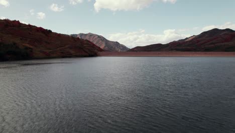 Toma-Aérea-De-Un-Dron-Volando-A-Baja-Altura-Sobre-Un-Lago-Para-Revelar-Una-Cadena-Montañosa-En-Salt-Lake-City-Con-Hojas-De-Colores-Otoñales-A-60-Fps