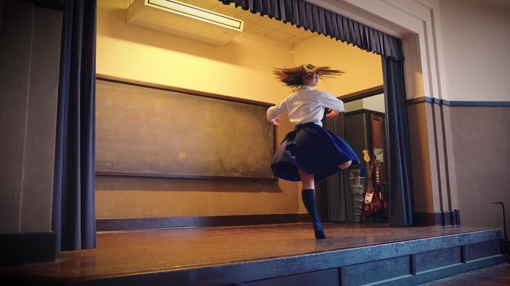 Ragazza giapponese delle scuole superiori in uniforme fa balletto sul palco della scuola.