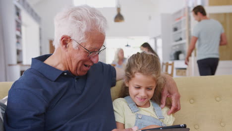 Abuelo-Sentado-Con-Su-Nieta-En-El-Sofá-Usando-Una-Tableta-Digital-En-Casa