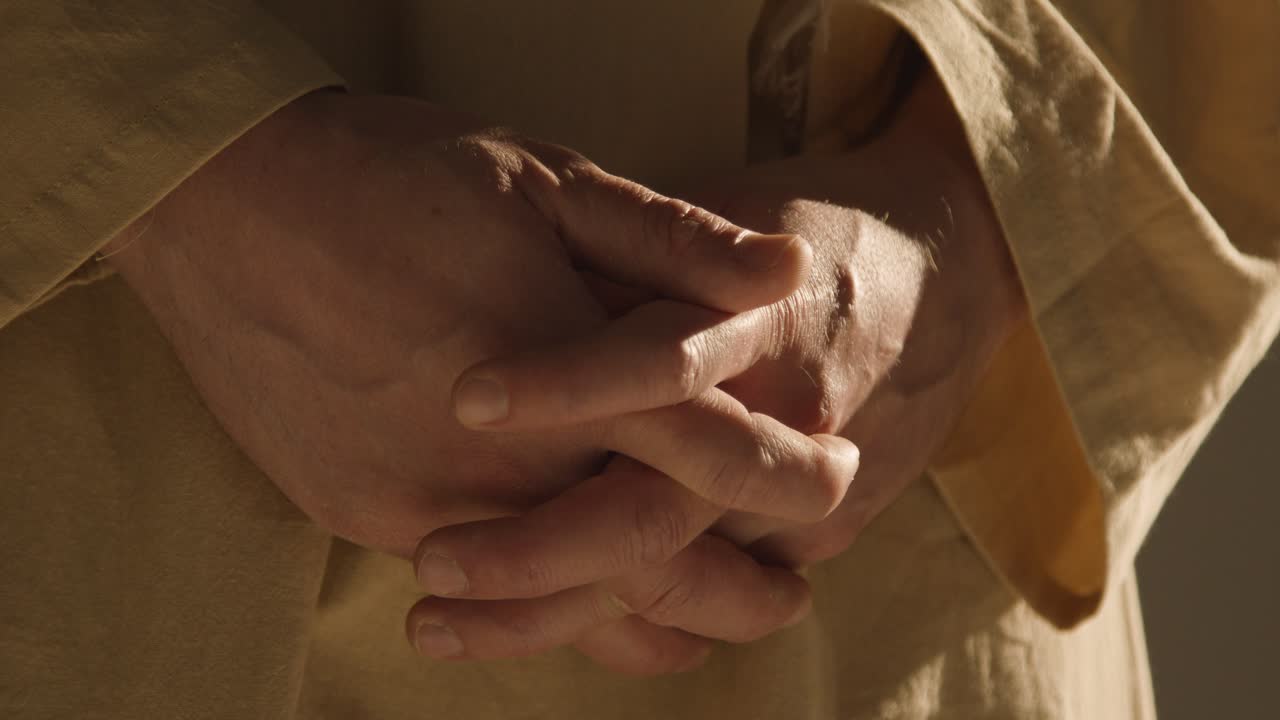 primer plano de un hombre vestido con túnicas que representan la figura de jesucristo con las manos juntas