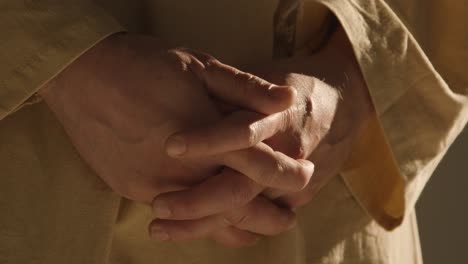 close up of man wearing robes representing figure of jesus christ with hands clasped together