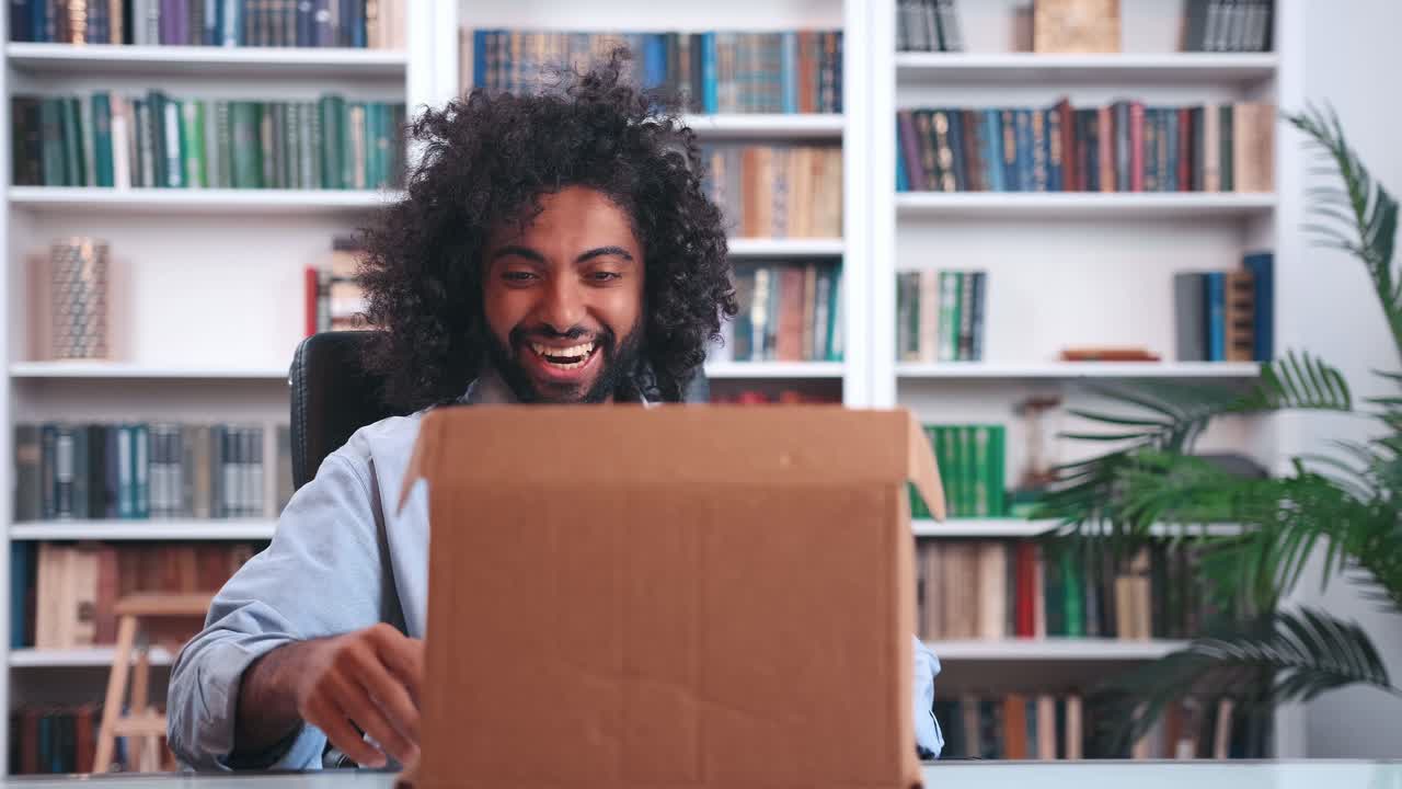 Excited overjoyed young indian man freelancer opens cardboard box and rejoices
