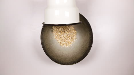 verter una taza de granos de avena en un recipiente para gachas de avena - toma cenital, cámara lenta