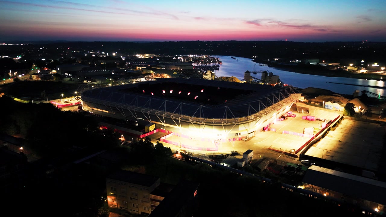Dronebilde av sterk utendørsbelysning rundt St Marys Stadium i kontrast til en rosa daggryhimmel og den mørke elvebredden ved River Itchen