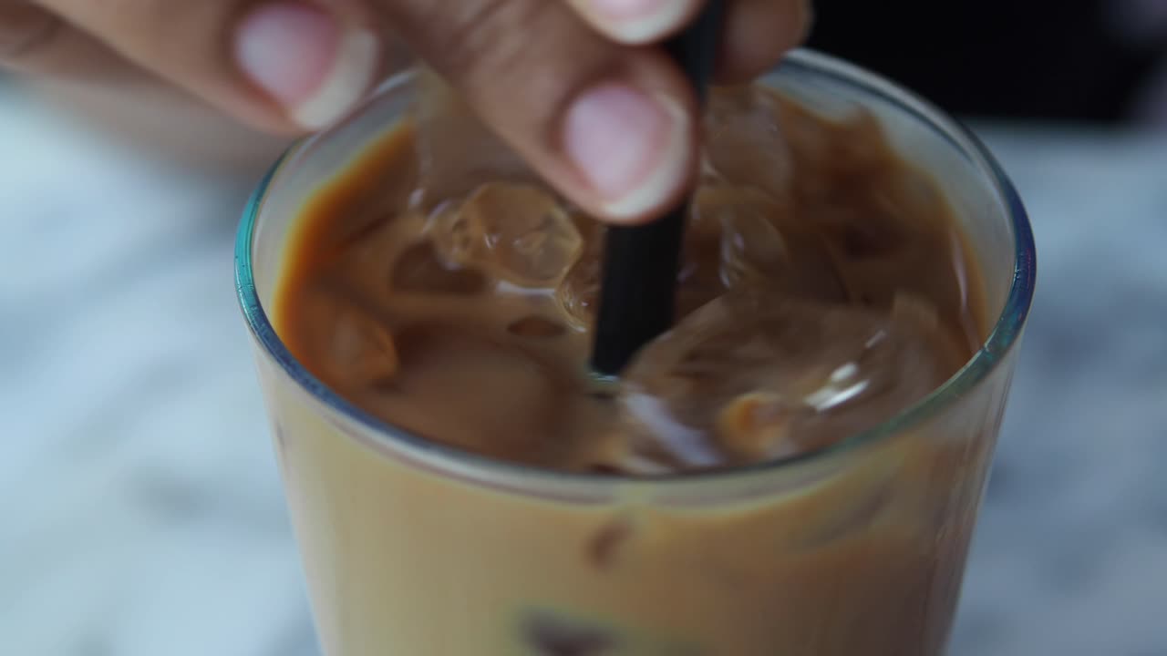 Mano removiendo café helado con una pajita en un vaso