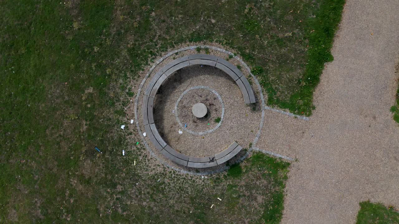 Top-down drone rise and rotate over C-shaped bench on grass and path