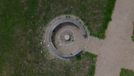 top-down drone rise and rotate over c-shaped bench on grass and path
