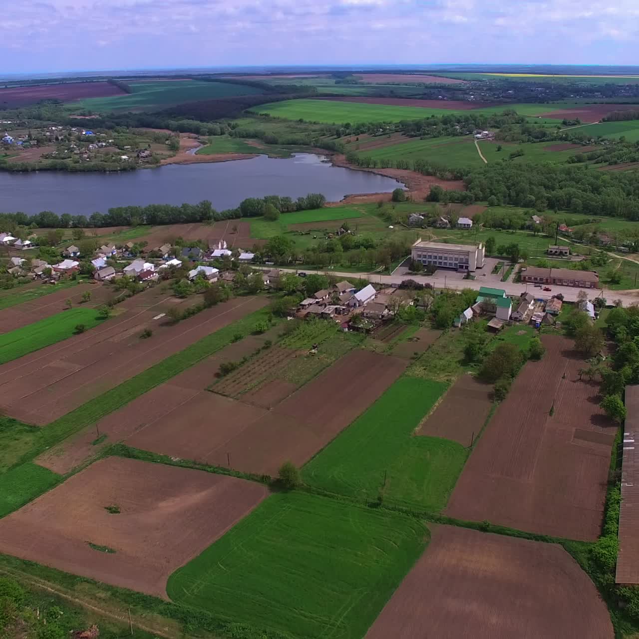 Beautiful scenery of rural area nearby little river. Drone footage over agricultural fields and green forests nearby. View from top