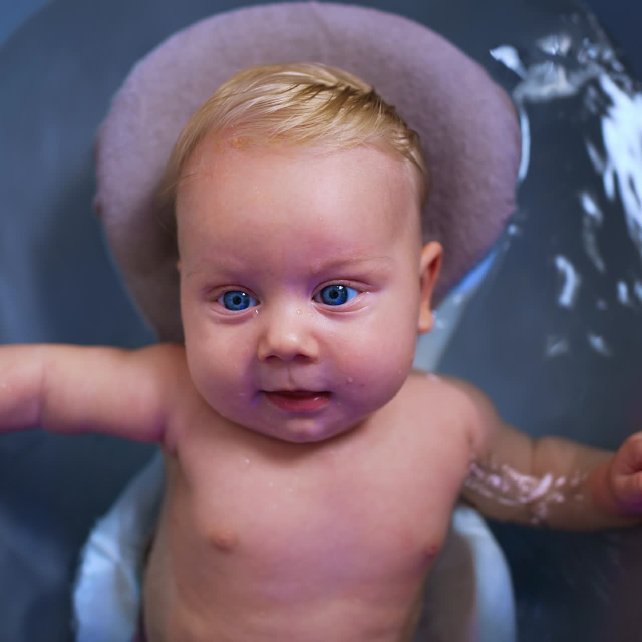 Søt, liten, blond baby med blå øyne i et badekar. Nærbildeportrett av et barn som koser seg i badet. Toppvinkel